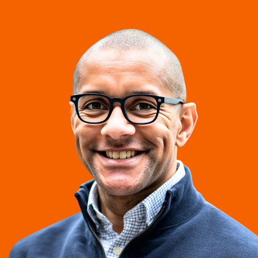 Wilfred Stephen Anfield, a Black man with a warm smile, wearing glasses and a blue quarter-zip sweater against an orange background